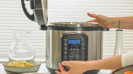 Modern electric multi cooker or Pressure cooker close up on kitchen table. Woman pushing button