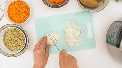 Lentil soup recipe. Chef chopping white onion, close up view from above