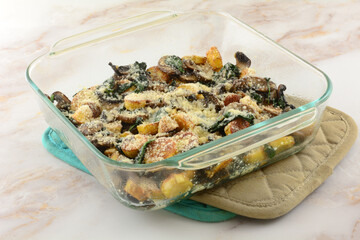 Baked cheese casserole of potatoes, spinach, and mushrooms in glass baking dish on two pot holders