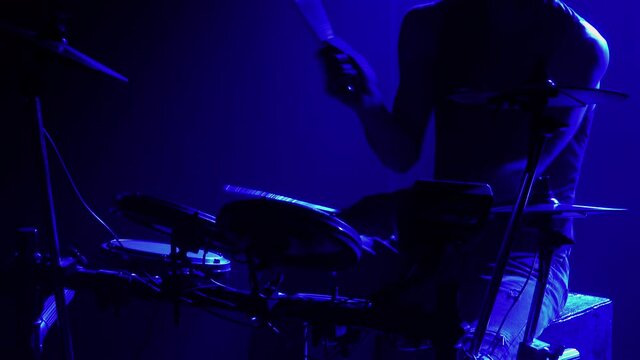 Professional musician playing drums and percussion cymbals in a dark smoky studio with blue lights. Close up of the drummer torso pounds on the drum kit. Rock concert, live performance. Silhouette.