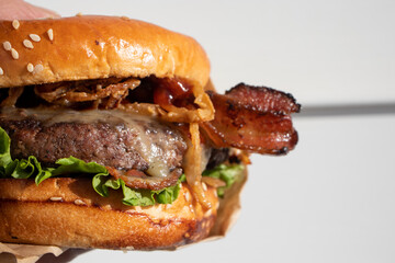 A freshly cooked, juicy western BBQ burger with cheese, fried, onions, lettuce, bacon, barbecue sauce on a sesame seed bun in front of a white background.