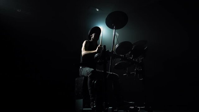 Bottom view of a rock musician playing drums and percussion cymbals. The drummer is a virtuoso master of drum sticks to create a cool live rock concert. Silhouette in the center of the beam of light.