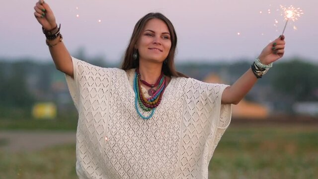 Attractive woman aged boho style. Portrait of brunette hippie with sparklers. Woman with sparklers on nature background