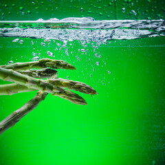 asparagus in water with splashes on a green background.