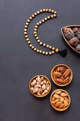 Fototapeta na wymiar Ramadan Kareem and iftar muslim food, modern holiday concept. Wooden bowls with nuts and dried fruits and the moon made of beads for rosary with tassel on a black background with copy space