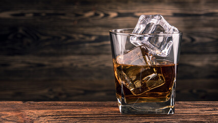 Glass of Whiskey, Bourbon or Brandy with ice cube on natural wooden background. Alcohol drink on Bar counter in the restaurant. Macro photo with copy space. 