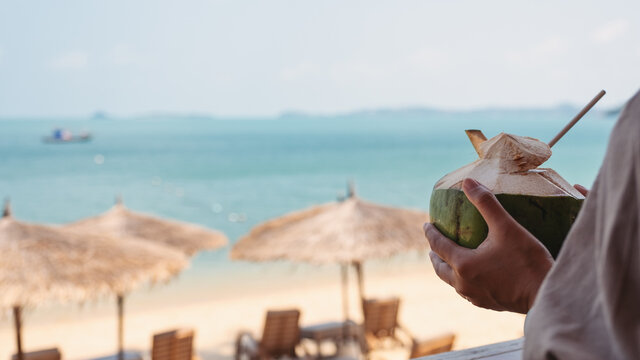 Closeup image a woman holding fresh coconut cocktail on the beach