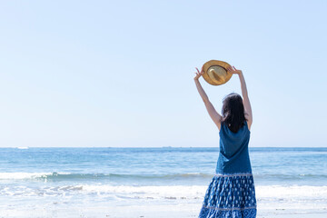 麦わら帽子を持ってストレッチをしながら海を眺める女性