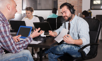 Young bearded man sharing business ideas with his senior colleague in open plan office. Concept of teamwork