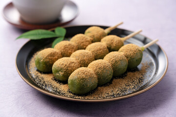 mugwort-flavored rice dumpling and green tea served on a black plate set against a purple background