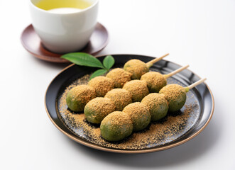 mugwort-flavored rice dumpling covered with soybean flour and green tea served on a black plate set against a white background.
