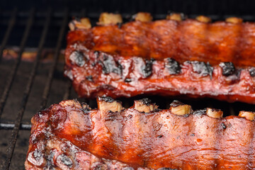 Close up of two racks of pork BBQ ribs brushed in BBQ sauce on a smoker grill
