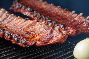 Close up of two racks of pork BBQ ribs brushed in BBQ sauce on a smoker grill