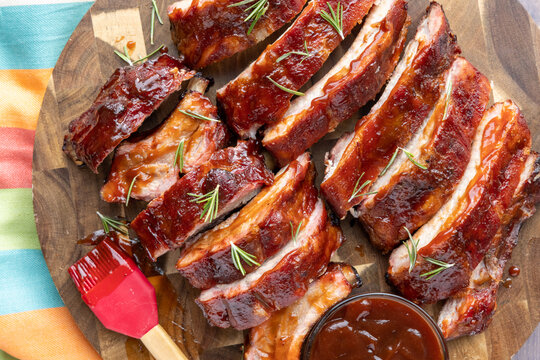 Overhead image of sliced smoked pork BBQ ribs on a board with BBQ sauce and brush