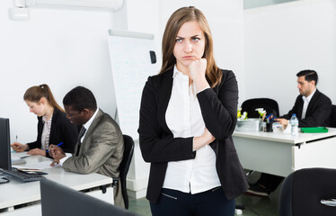 Portrait of frustrated young business woman in coworking space with working colleagues behind