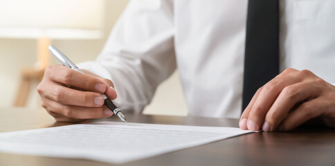 Businessman holds pen and signs agreement contract on the table.
