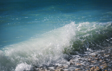 Turquoise blue sea wave crashes on a pebble shore, nature background and texture