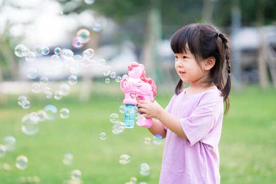 Child play with the bubble gun and have fun. Happy children standing in the grass. Sweet smile of a little girl. Time to relax. Summer or spring. Kid wearing a pink shirt is 4 years old.