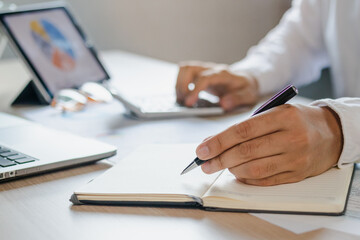 Young employee, businessman write note on laptop computer, touchpad, analyzing charts on paperwork...