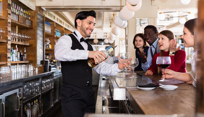 Portrait of positive barman and cheerful glad people who are standing near bar counter in luxurious...