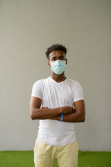 African man wearing face mask against plain wall background with arms crossed