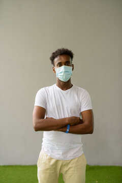 African Man Wearing Face Mask Against Plain Wall Background With Arms Crossed