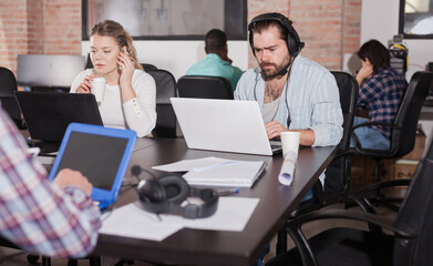 Latin hipster guy attentively watching webinar online using headset in modern coworking space