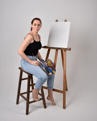 Full length portrait of a red haired artist girl wearing casual jeans and white shirt.  Sitting...