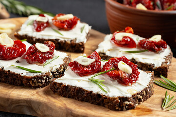 Homemade multigrain bread sandwiches with cream cheese and sun-dried tomatoes on a wooden platter, close-up. Healthy eating concept