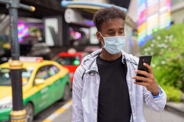 African man wearing face mask and using phone at taxi station