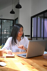 Portrait of woman accountant in eyeglasses using calculator and working with laptop computer at office desk.