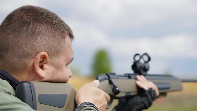 Portrait man in camouflage clothes with rifle shooting outdoors alone, close up