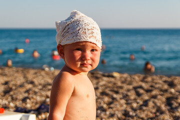 one-year-old baby girl in bandanna stands on the beach in Turkey in the summer