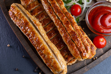 lula kebab made of chicken on a wooden board with pickled onions, chili peppers and cherry tomatoes on a dark background. photos with a small depth of field