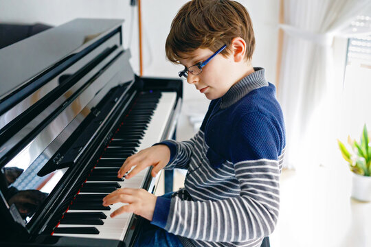 School boy with glasses playing piano in living room. Child having fun with learning to play music instrument. Talented kid during homeschooling corona virus lockdown.