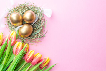 Easter Golden eggs in basket with spring tulips, white feathers on pastel pink background in Happy Easter decoration. Spring holiday flat lay concept.
