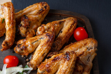 grilled on coals chicken wings on a wooden board with pickled onions, chili peppers and cherry tomatoes on a dark background. photos with a small depth of field, top view