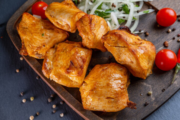 grilled chicken shish kebab shashlik on a wooden board with pickled onions, chili peppers and cherry tomatoes on a dark background