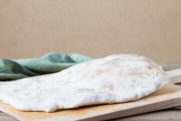 A homemade white puffy tortilla sits on a wooden bread shovel.