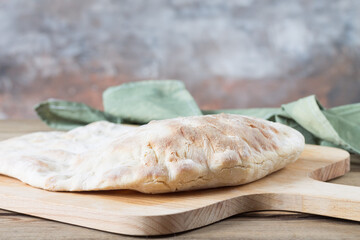 A homemade white puffy tortilla sits on a wooden bread shovel. Bread with flour sourdough.