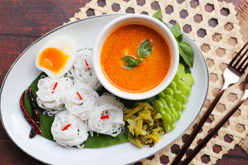Thai rice noodles with fish curry sauce , fish ball, boiled egg and vegetables and , Thai food called Kanom Jeen Nam Ya - Top view on wood table