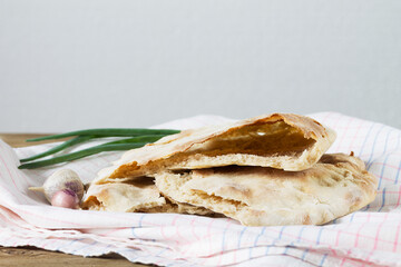 The broken pita bread on flour sourdough lies on a table towel together with green onions and garlic.