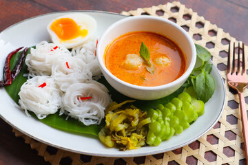 Thai rice noodles with fish curry sauce , fish ball, boiled egg and vegetables and , Thai food called Kanom Jeen Nam Ya - close up view on wood table