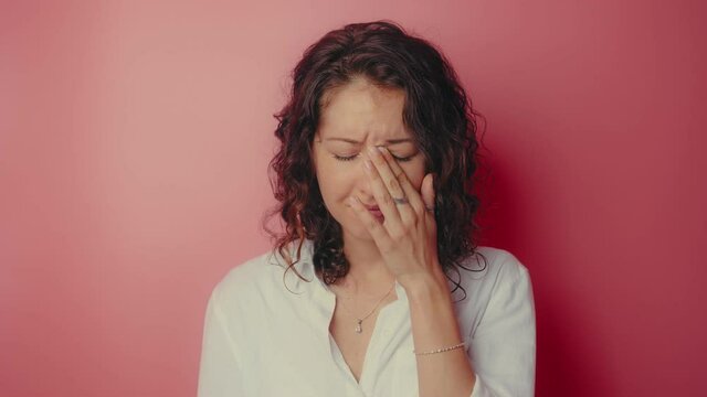 Young attractive girl desperately crying on a pink wall background