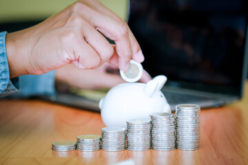 Business men put the coins into the white piggy bank and the coins stacks were lined up in front. The idea of ​​saving money to be used in the future. Financial and business concept