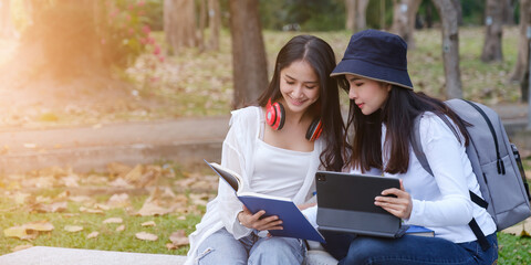 Two students are sitting in park during reading a book and communication. Study, education, university, college, graduate concept.