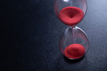 Sand passes through an hourglass, measuring the travel time counting down to the deadline, against...