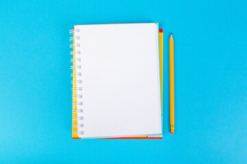 school notebooks on a blue background, spiral notepad with a blank page and a pencil on the table top view