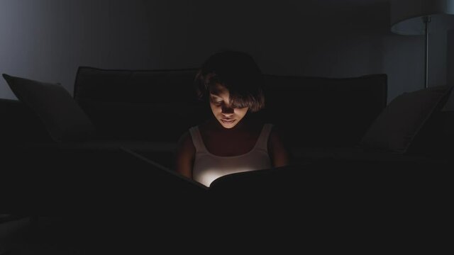 Portrait of young female sitting at home on the floor and reading a book, warm light, self-isolation during the pandemic, mystical lighting effect.