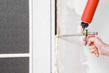 Young adult man hand using spray gun and filling gap with construction foam between new glass...